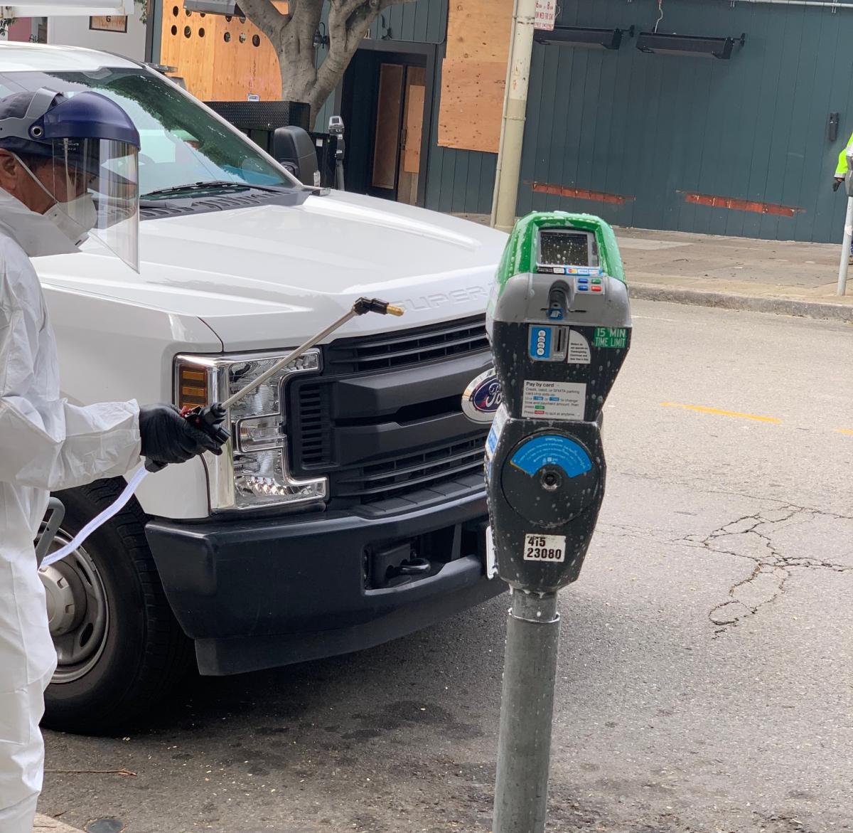 Parking Meter being sanitized by someone in a safety suit with visor