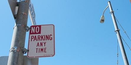 No Parking Any Time sign mounted on street pole against clear blue sky.