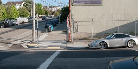 Silver car parked away from marked crosswalk at street corner.