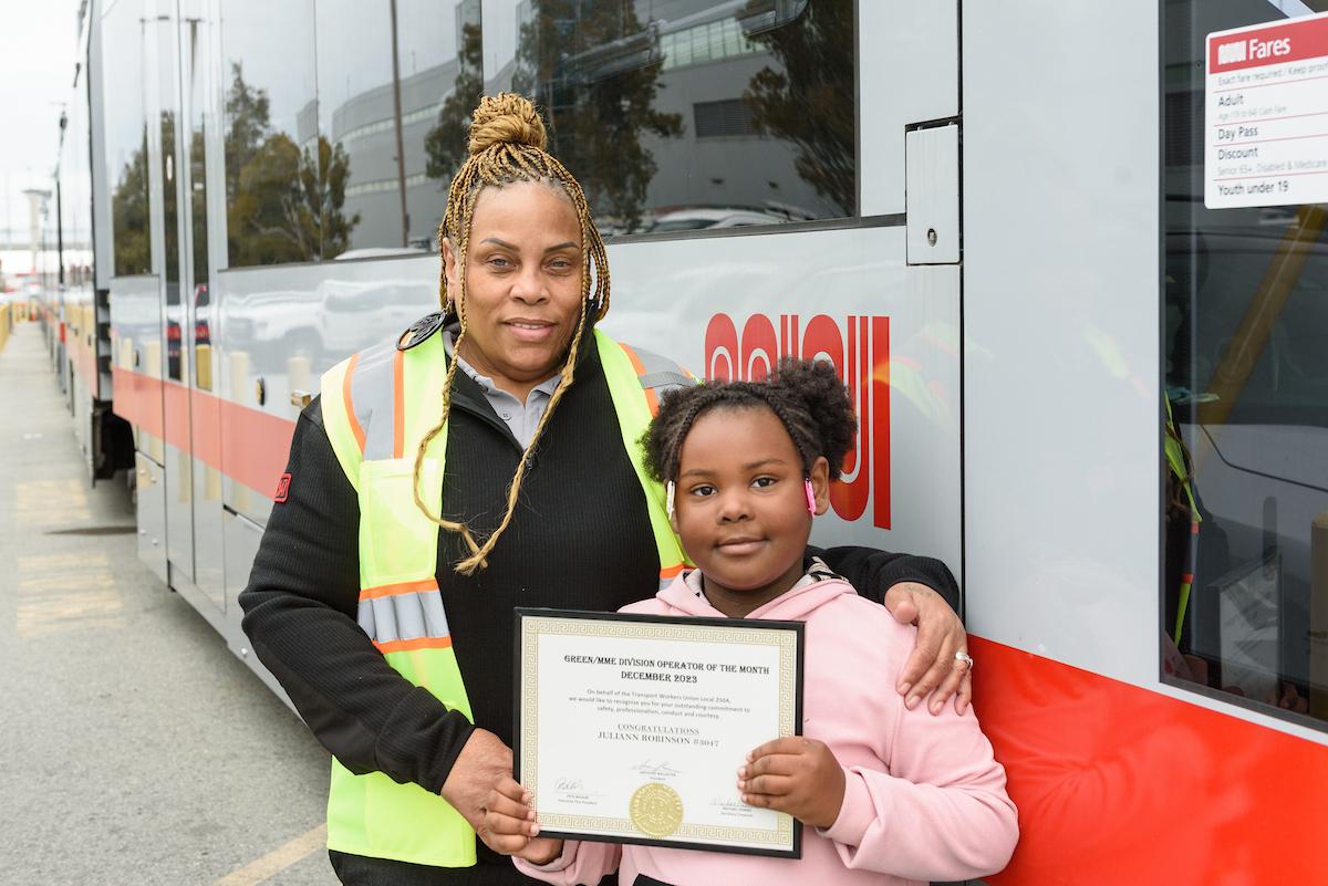 A woman and child standing in front of a train and holding a certificate.