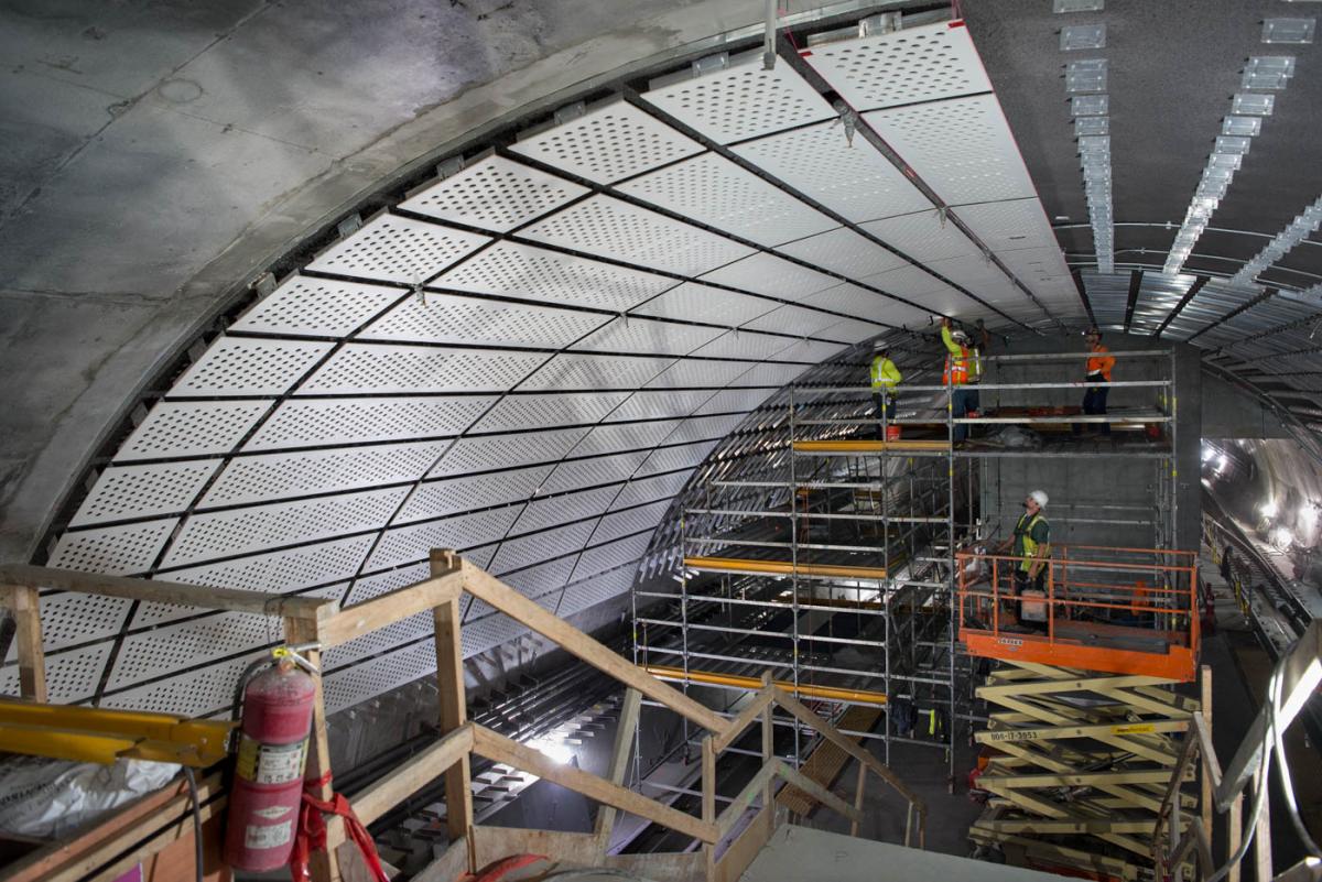 Sound reduction panels are being attached to steel brackets mounted to the arched concrete ceiling of the Chinatown-Rose Pak Station platform cavern.