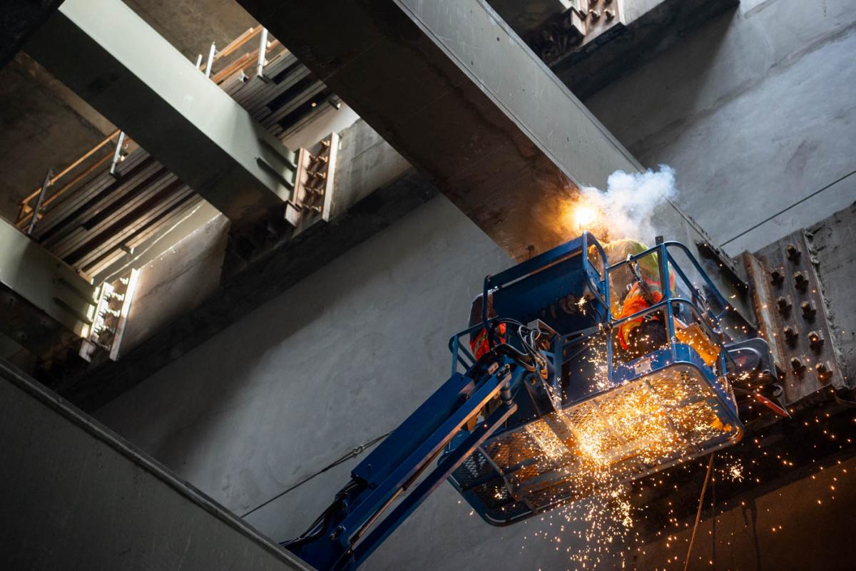 Sparks fly as workers weld brackets to massive steel beams inside the Chinatown - Rose Pak Station entrance structure.