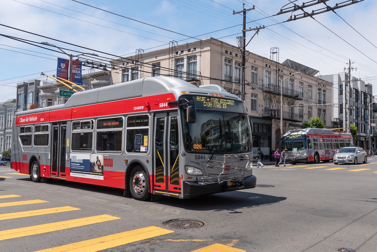 photo of two Muni buses at intersection with pedestrians in the crosswalk