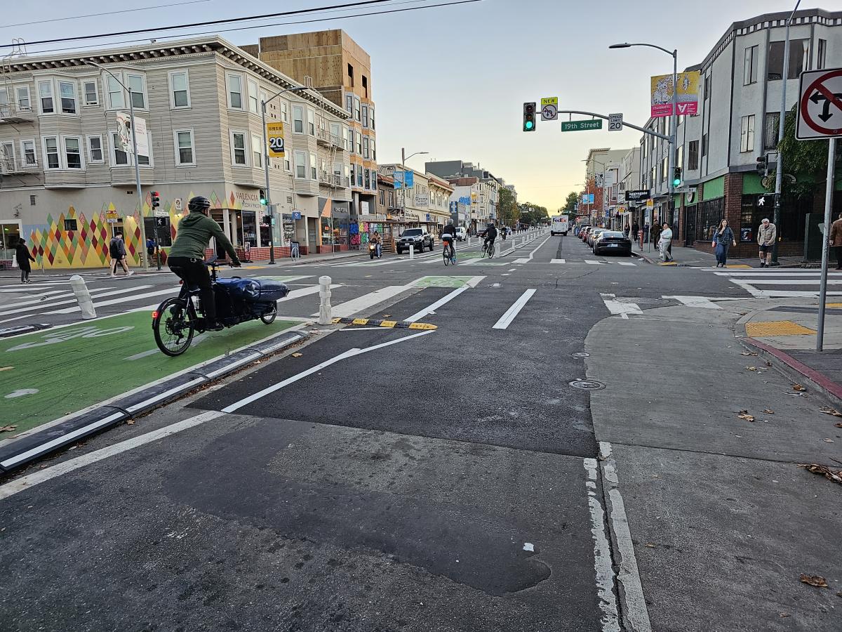 A woman bikes on a green bike lane, the new center-running design on Valencia Street. She follows other cyclists on the corridor.