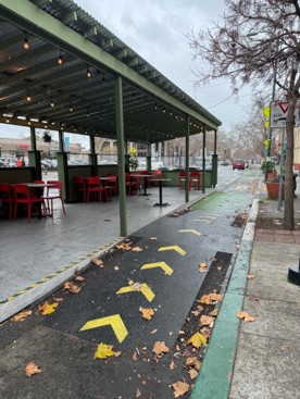 Photo shows a floating parklet in Oakland where there is a bike lane located between the curb and a large parklet with tables and chairs.  
