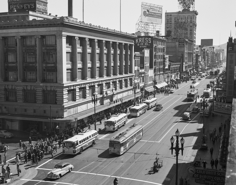 Black and white photo showing a view from above looking west/south west on Market Street from Eddy Street showing buses, streetcars, and pedestrians traveling on the street. Taken in July 1947.