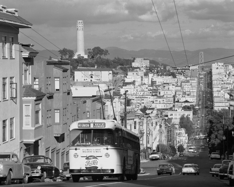 Black and white photo taken October 4, 1957 showing an electric trolley bus climbing Russian hill on Union Street. In the background is the North Beach Neighborhood and Coit Tower.