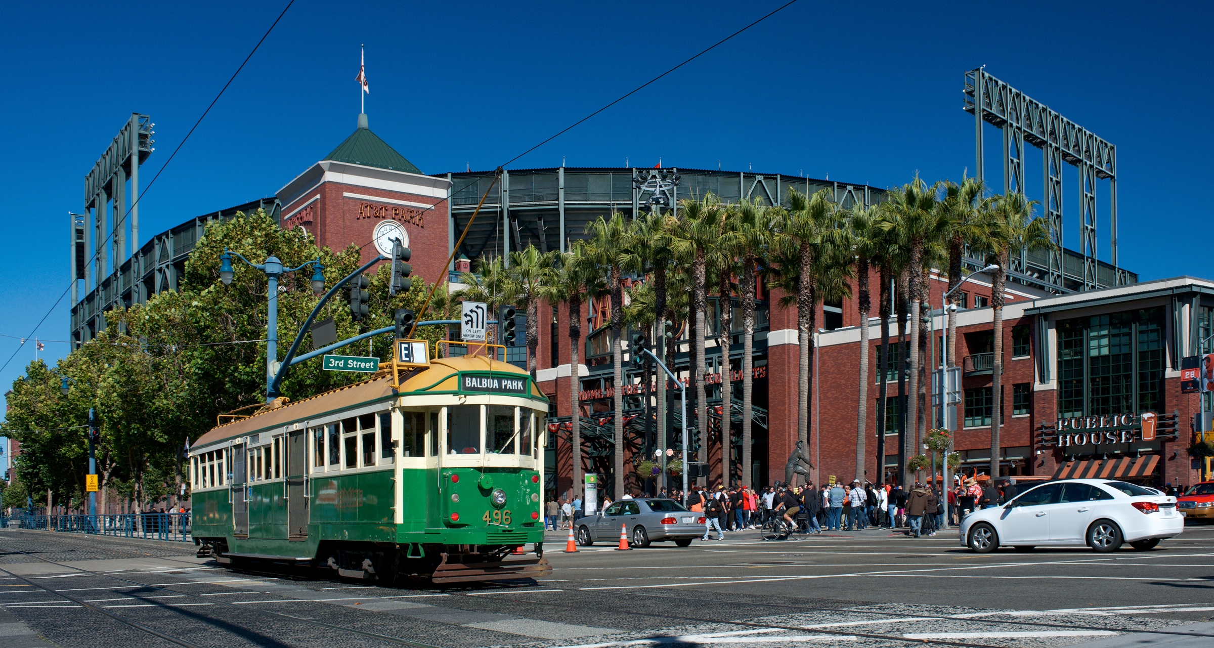 AT&T Park with baseball fans crowded in front and a green and cream F Line car #496 travling west on King in front of the park