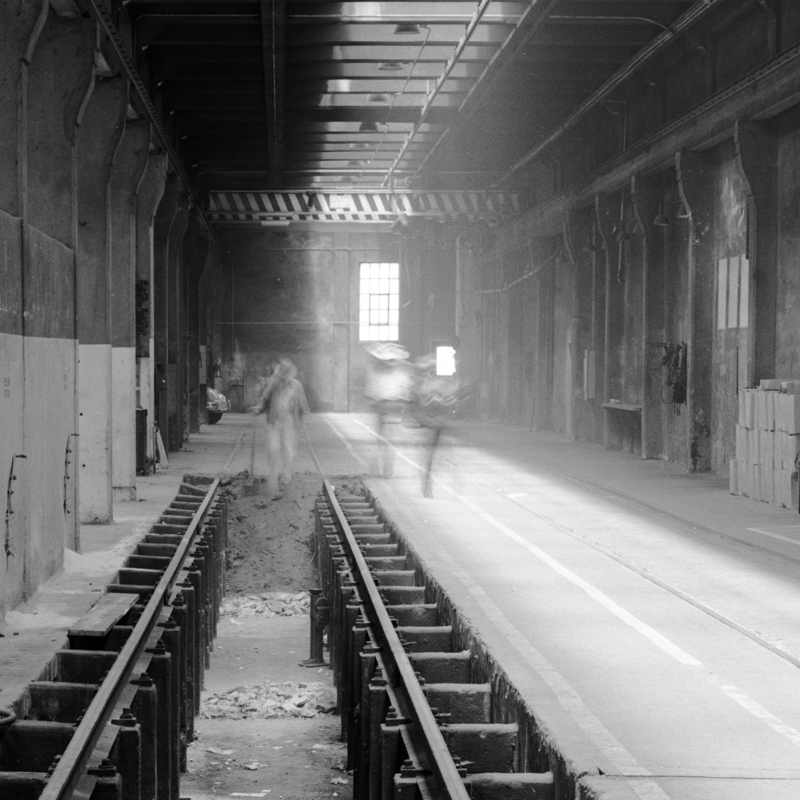 Black and white photo from the 1940s showing the interior of Presidio Carhouse with blurred figures walking around a pit with rails.