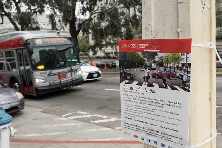 Bus driving up Van Ness Avenue, foreground is a construction notice posted for the Van Ness Improvement Project.