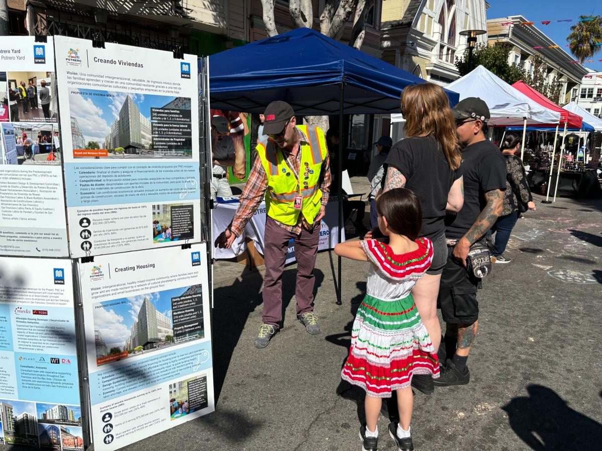 people stand outside looking at boards with information about the Potrero Yard Modernization Project