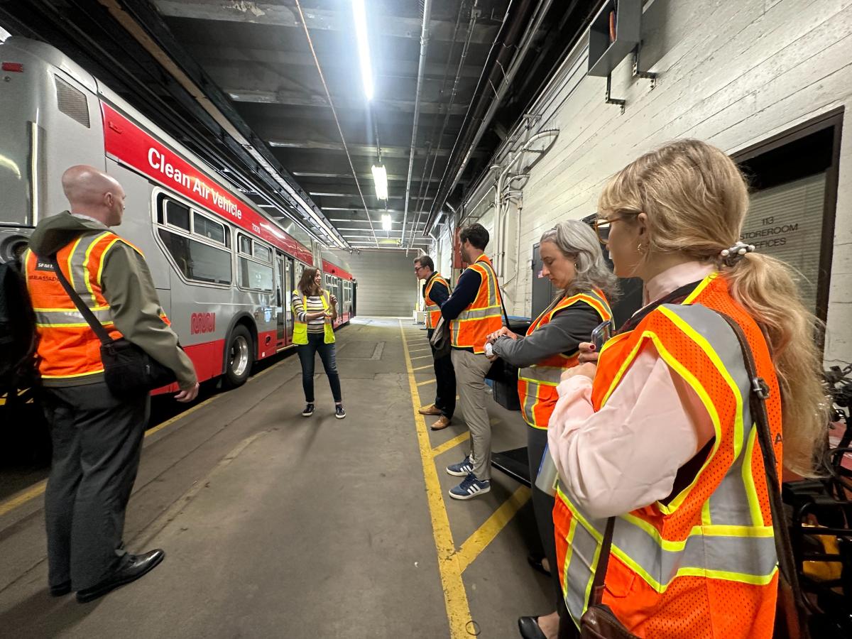 six people stand near a bus inside the Potrero Bus Yard