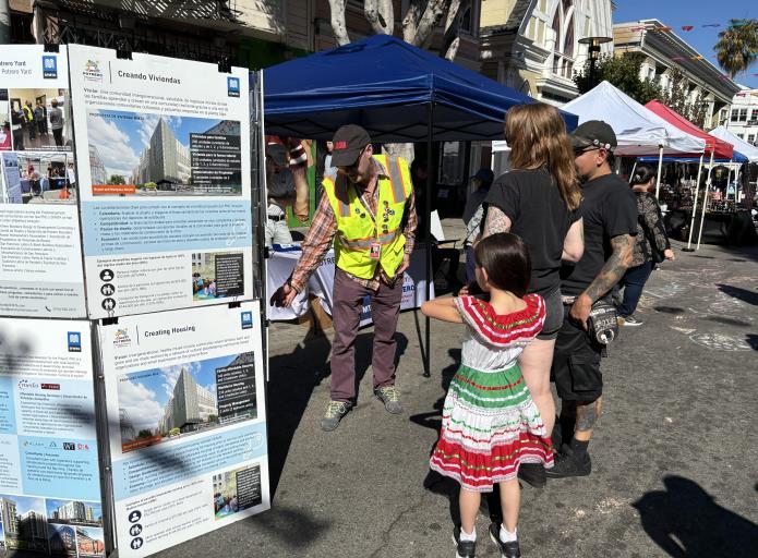 a group of people in colorful clothing look at an informational board in an outdoor setting.