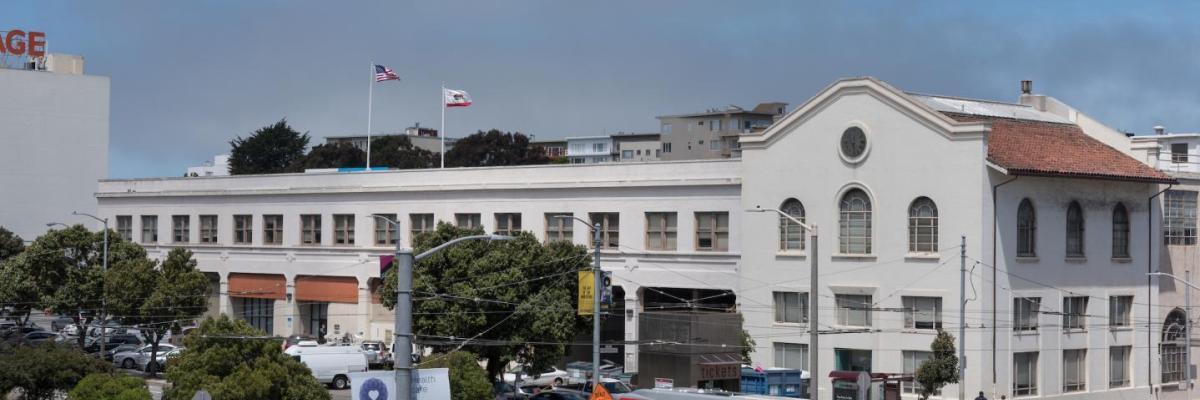 the front of presidio yard. white building with a clock and red roofing