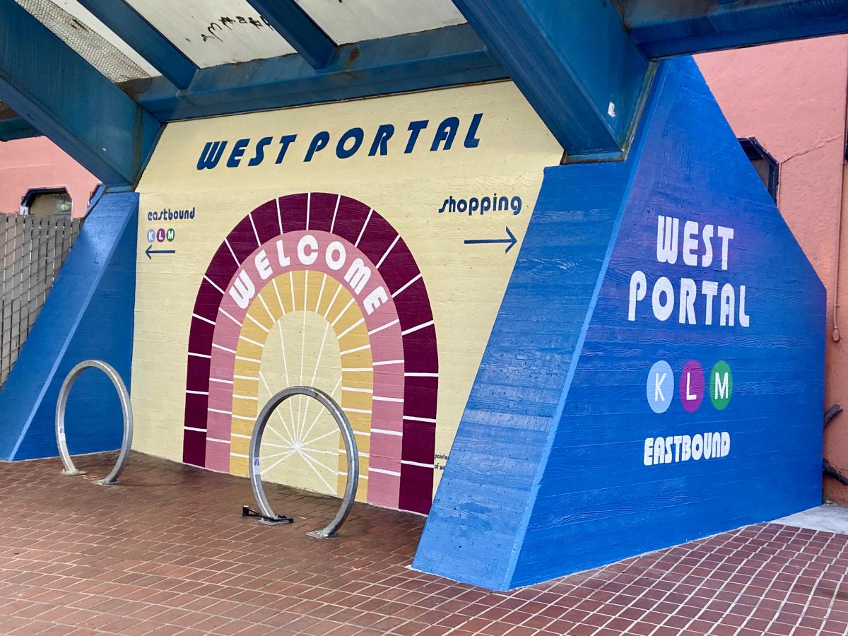 A mural on the wall of West Portal Station shows 'welcome' over an illustration of the tunnel and directs passengers to inbound and outbound platforms.