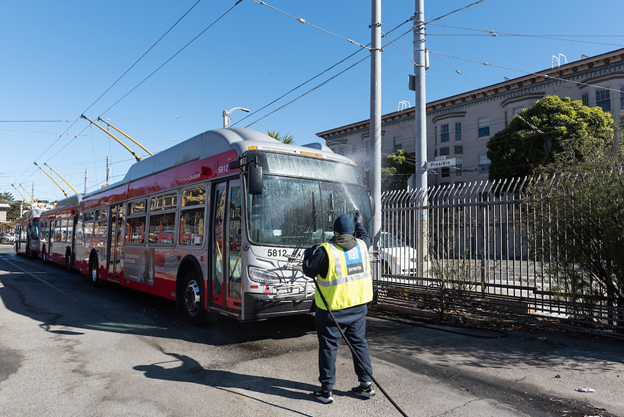 A silver and red trolley bus attached to overhead wires with an employee in a yellow safety jacket looking on.