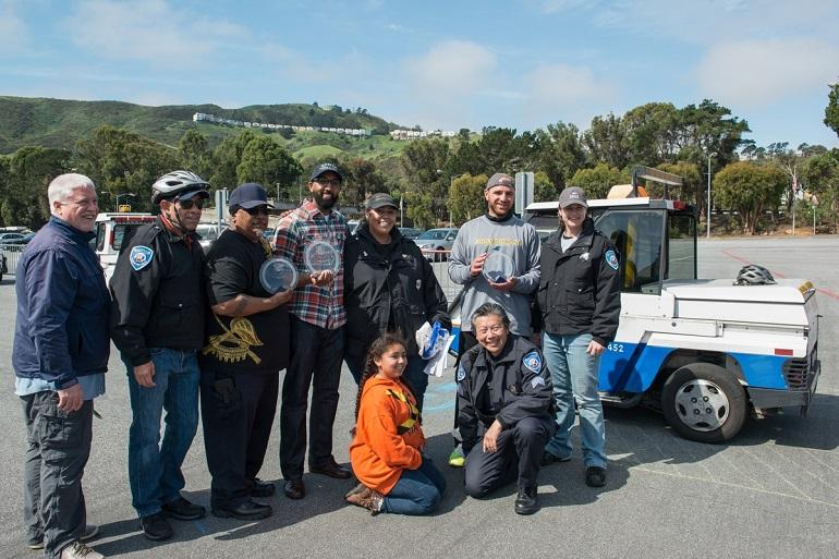 Group of transit workers and parking control officers posing together next to a blue and white Muni vehicle at a safety roadeo event.