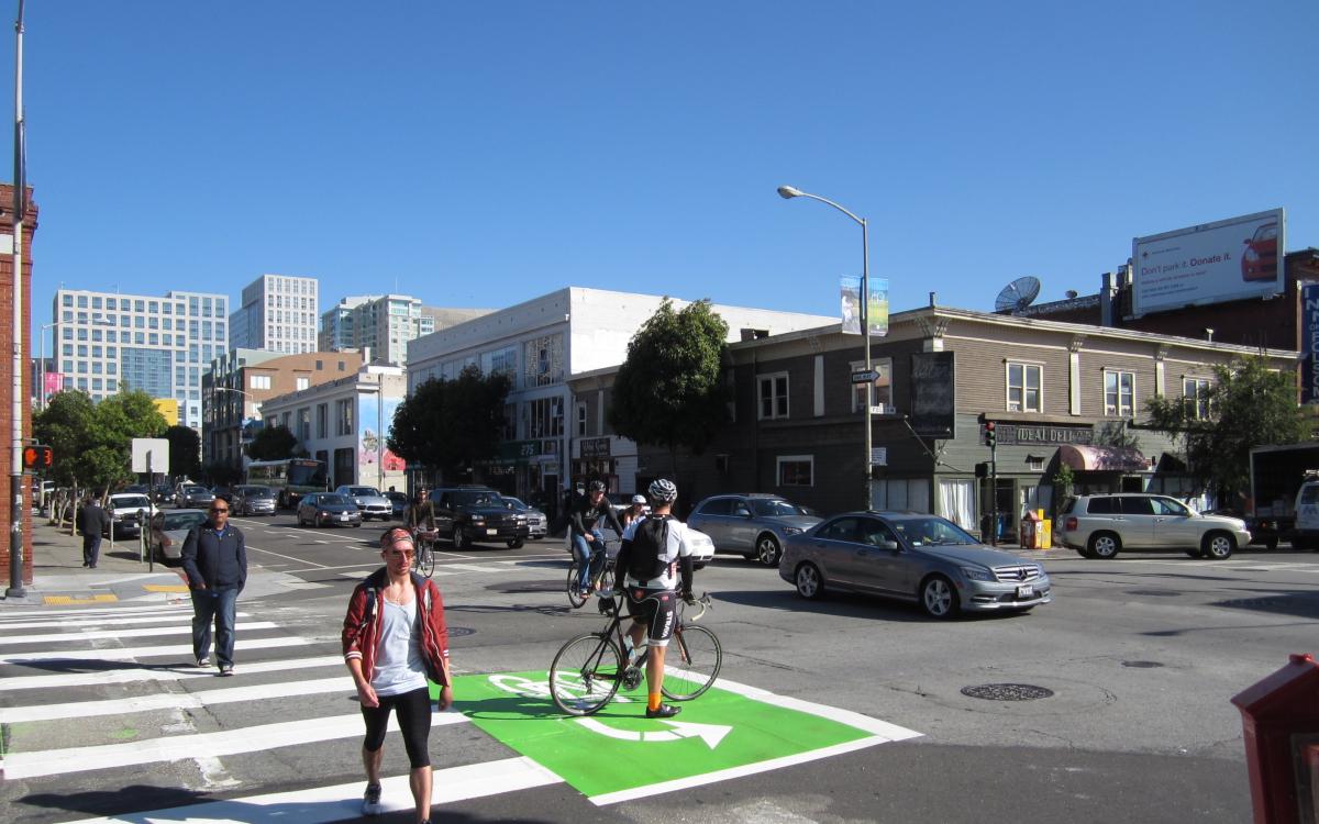 Cyclist in green bike box at urban intersection with pedestrians and vehicles