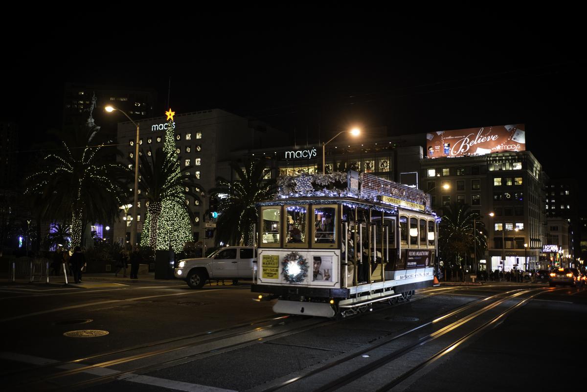 Cable car decorated with holiday lights traveling on Powell Street at night near Union Square and Macy's.