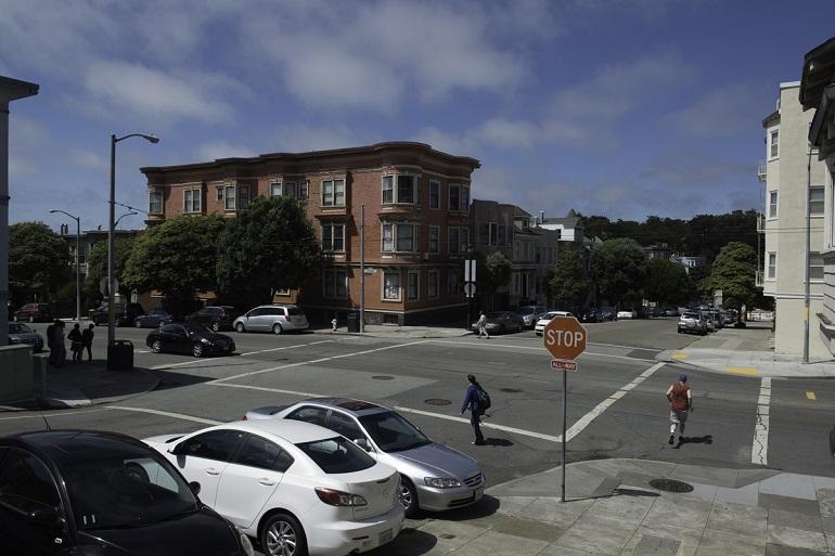 Irving Street intersection in San Francisco's Inner Sunset neighborhood with brick building, parked cars, and pedestrians at stop sign.