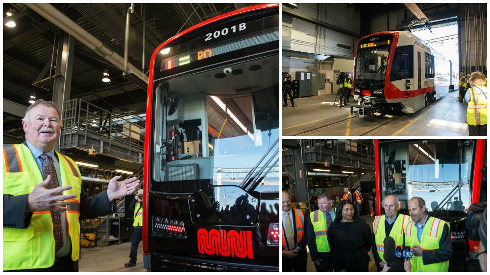 Officials and staff gather at a press event in front of a new red and white Muni light rail vehicle numbered 2001B.