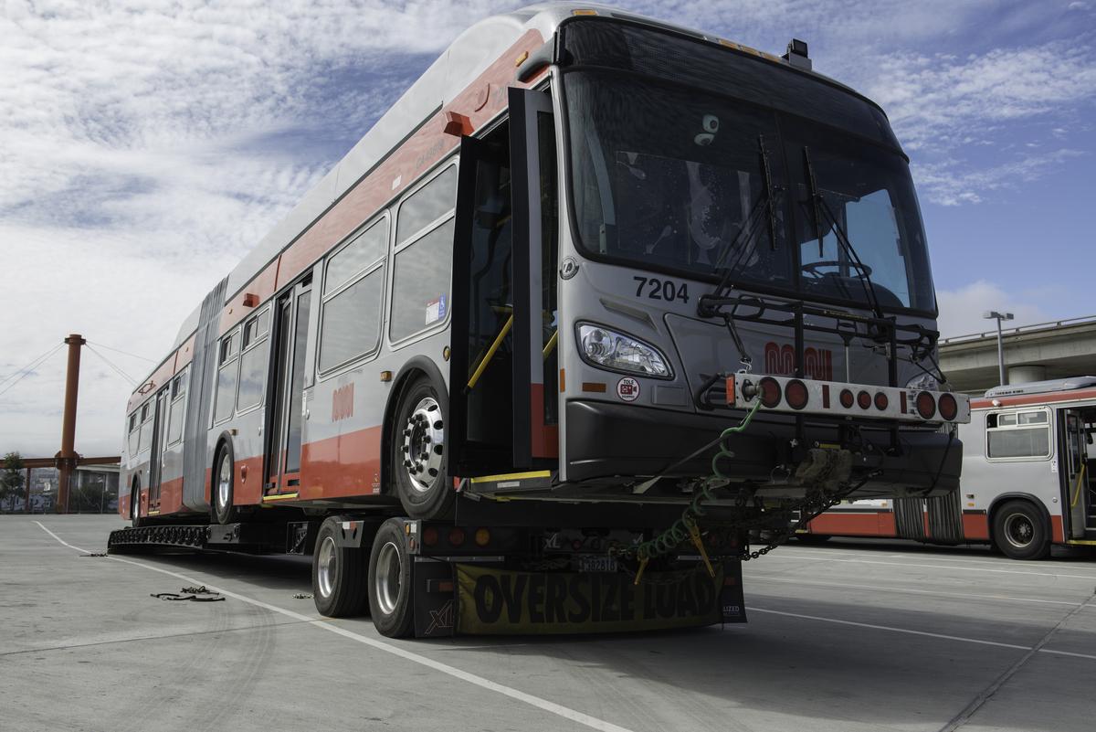 New Flyer articulated trolley coach 7204 being transported on a flatbed truck with oversized load banner.