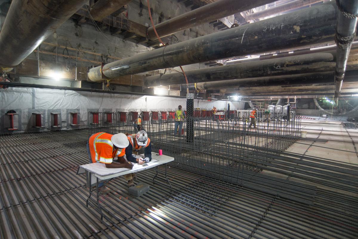 Construction workers install rebar for invert slab at underground transit station.
