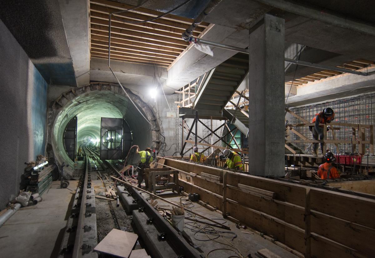 Construction workers build track infrastructure inside a subway tunnel under bright work lights.
