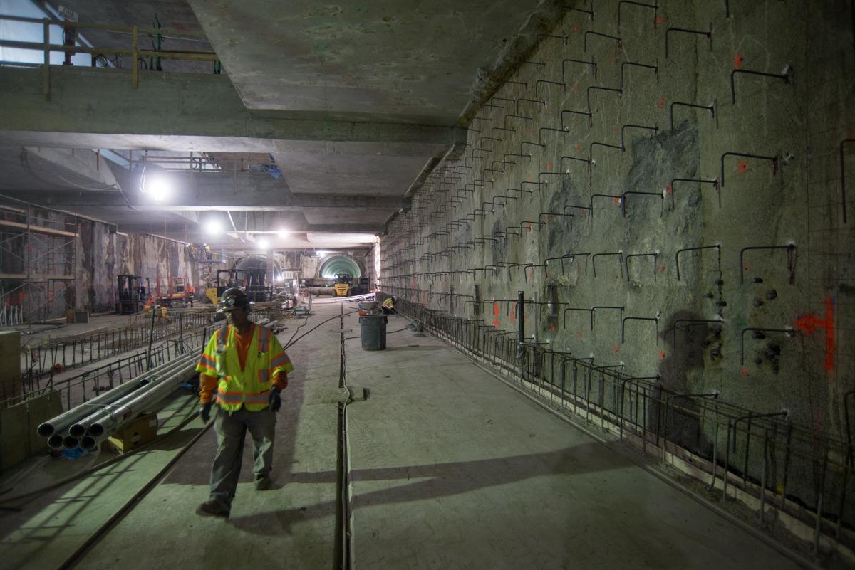 Worker in yellow safety vest inside underground station box during construction with concrete walls and rebar.