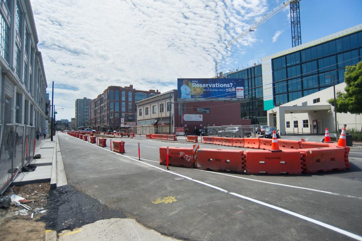 Construction site on 4th Street with red barriers dividing traffic lanes, modern buildings visible in background.