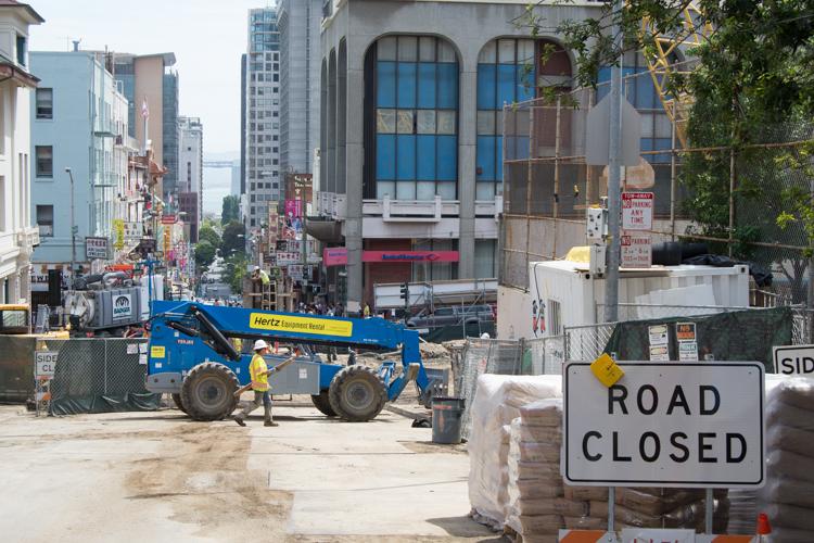 Construction site at Chinatown Station with road closed sign, blue Hertz equipment lift, and workers on Washington Street.
