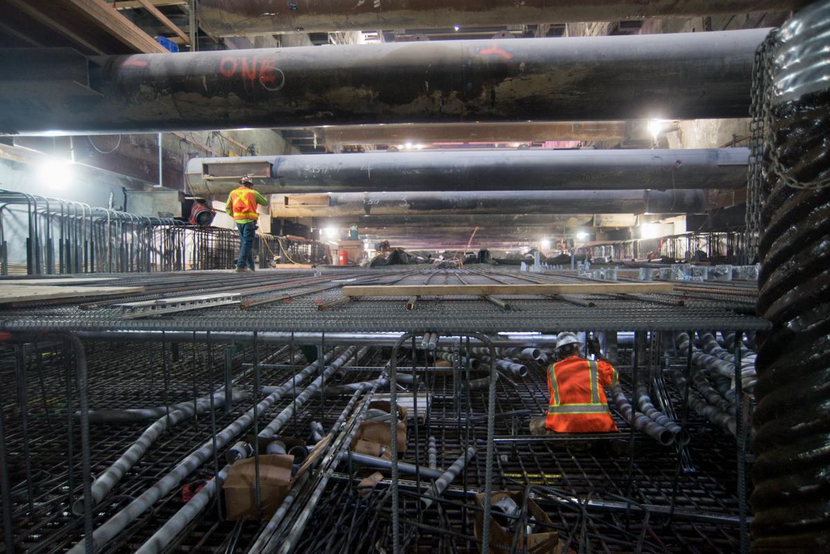Workers in safety vests on reinforced steel framework during Central Subway station construction underground.