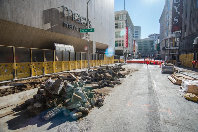 Construction site on Stockton Street with demolished roadway, yellow barriers, and building materials.