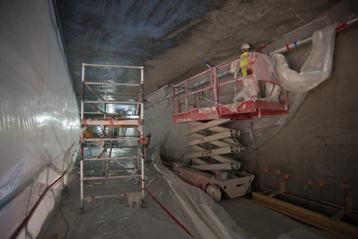Workers apply soundproofing material inside underground transit station under construction.
