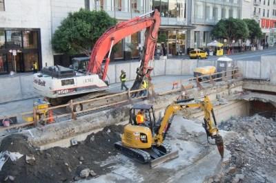 Construction equipment excavating underground at Union Square Garage site with buildings in background.