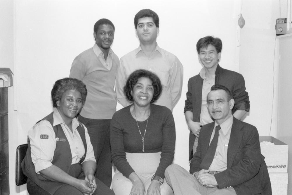Group photo of employees. The back row of three staff is standing. The front row of three staff is seated. One emplyee is wearing a Muni work vest.