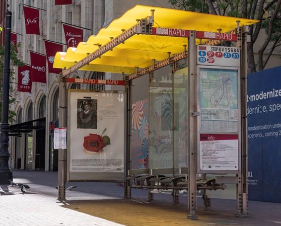 Photo of a bus shelter with an ad panel and yellow roof.