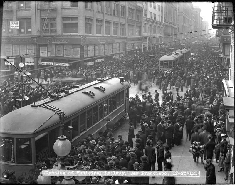 crowd of people with streetcars in street in 1912