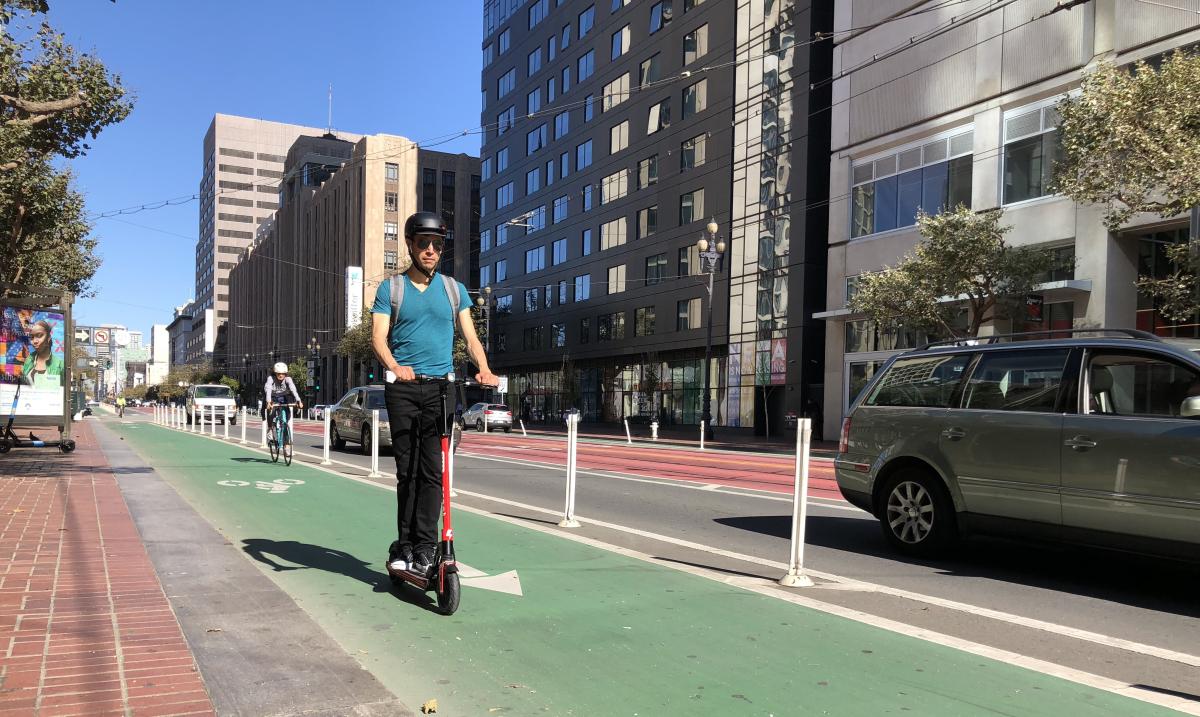A person wearing a helmet rides a scooter in a bike lane