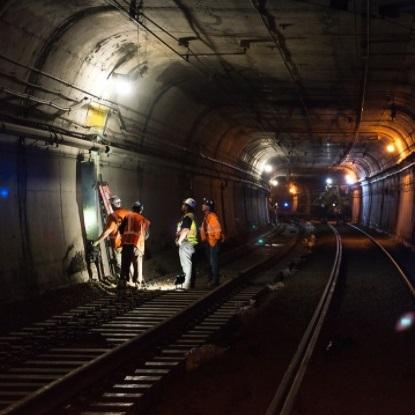 Photo showing 4 construction crew members working in subway tunnel on electrical connections