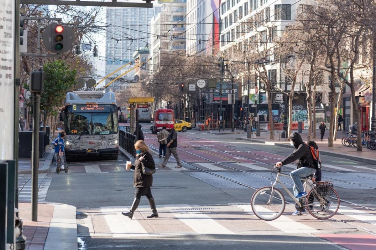 Photo of Market Street intersection with 5 Fulton bus, pedestrians, people on bicycles, a taxi, an ambulance, bikshare station, 