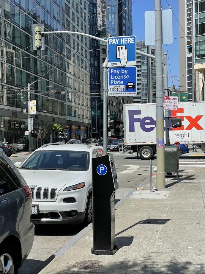 Photo of pay by license plate sign with paystation and parked cars