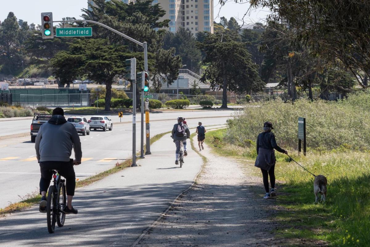 Photo of pedestrians, people on bicycles, and cars on Lake Merced Boulevard
