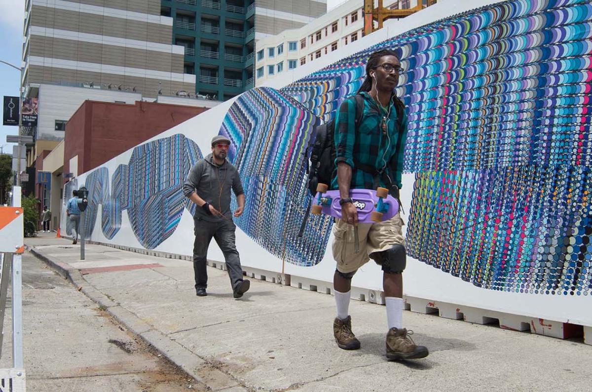 Two people walk by a mural consisting of overlapping circles of various colors