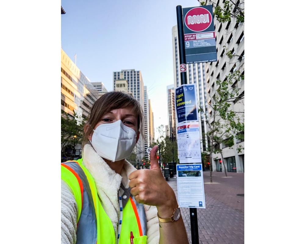 Photo of SFMTA staff giving a thumbs up after posting face mask, wayfinding, and ETC signs at a bus stop on Market Street.