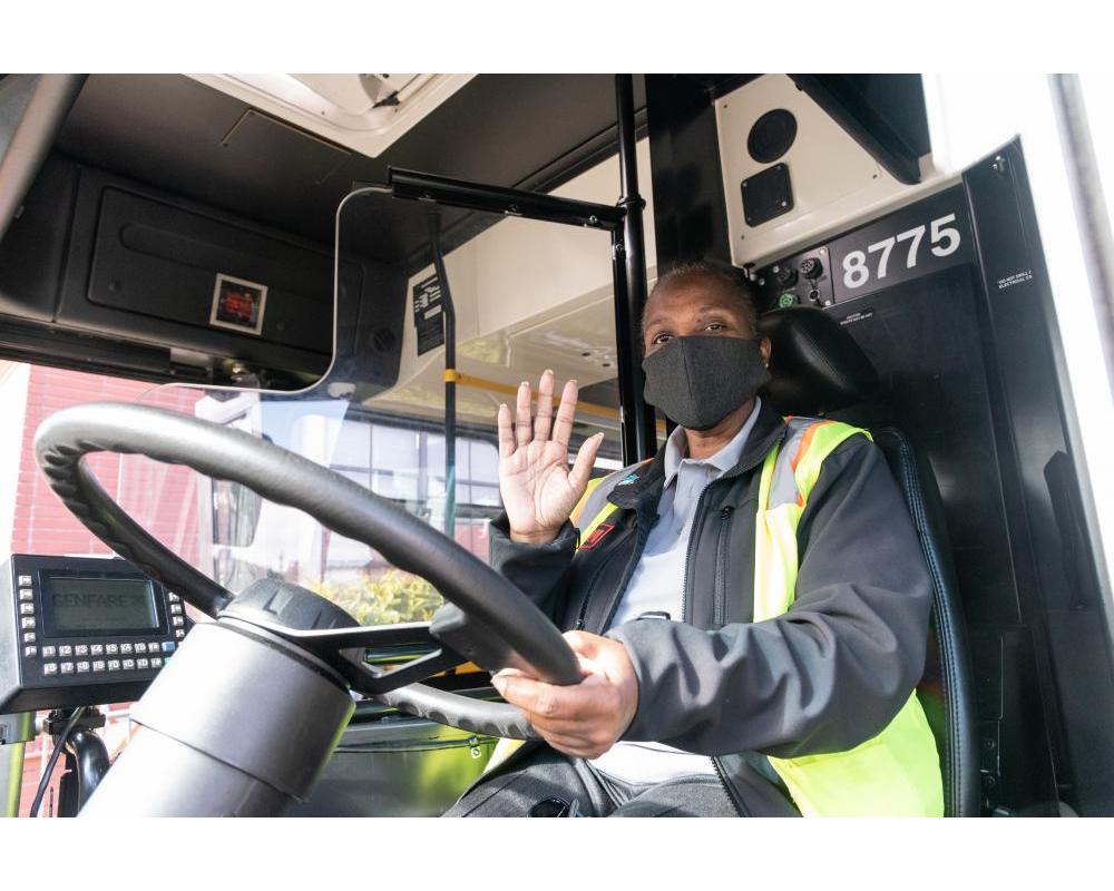 Operator waiving hello at the wheel of a bus