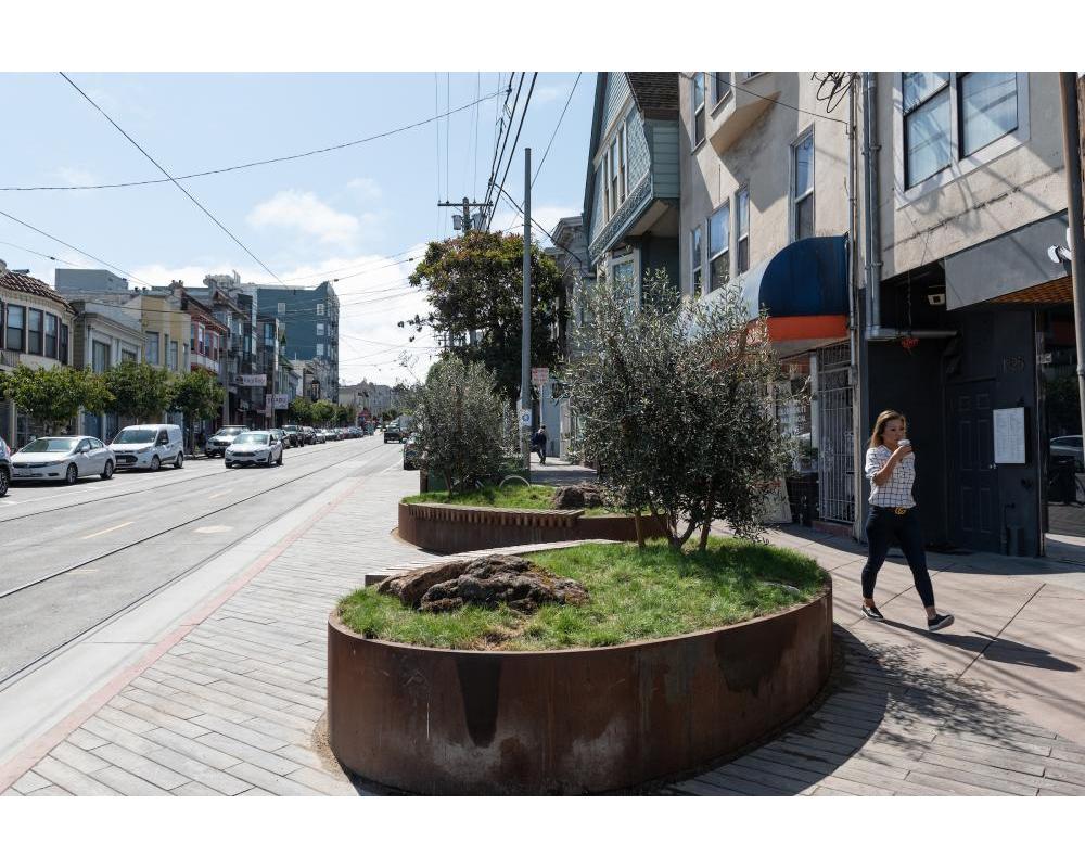 A person drinking coffee walks passed planters on a landscaped transit bulb