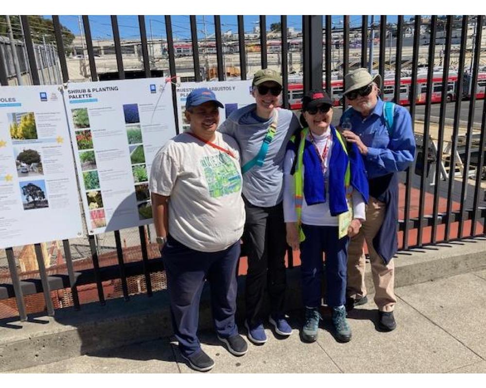 a group of people stand before a tall iron fence in front of informational boards. They smile at the camera. 