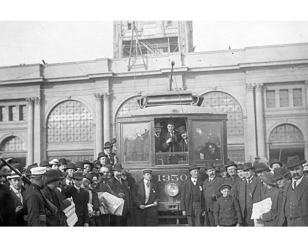 black and white photo of a crowd of people standing in front of a streetcar at the foot of the ferry building