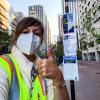 Photo of SFMTA staff giving a thumbs up after posting face mask, wayfinding, and ETC signs at a bus stop on Market Street.